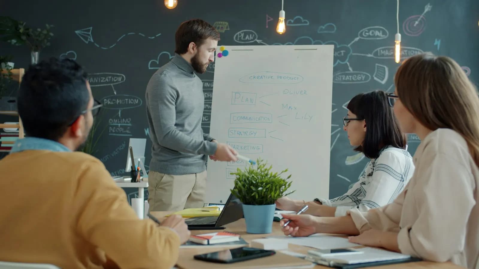 A team at a whiteboard in a modern office, one presenting to three colleagues