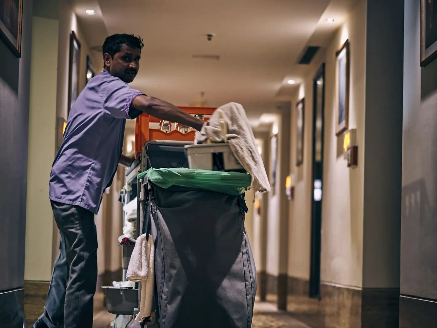 A housekeeping attendant moving a linen and supplies trolley along a corridor