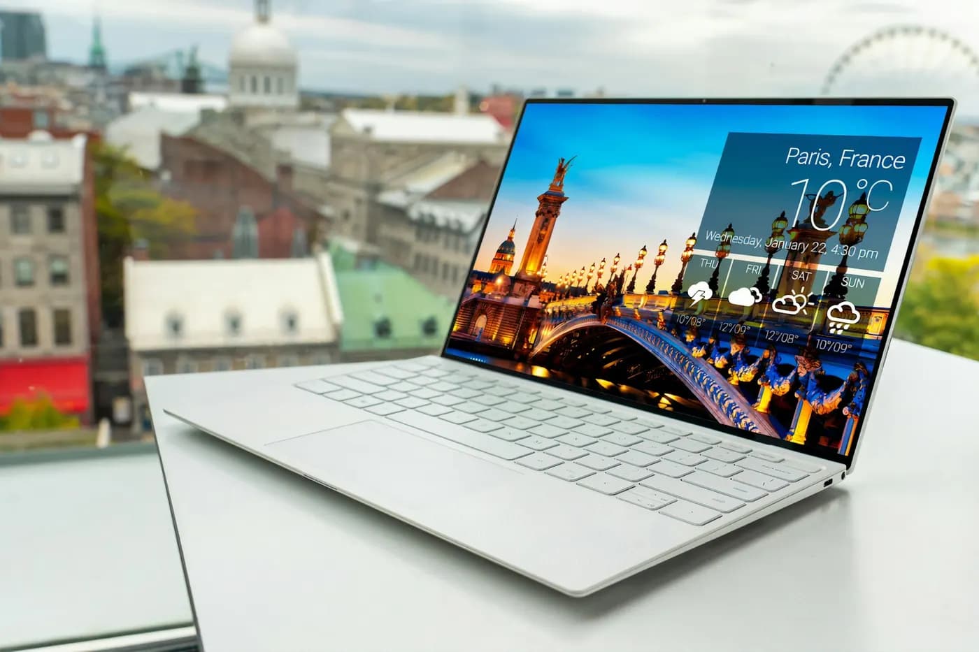 A thin business laptop open on a desk beside an office window
