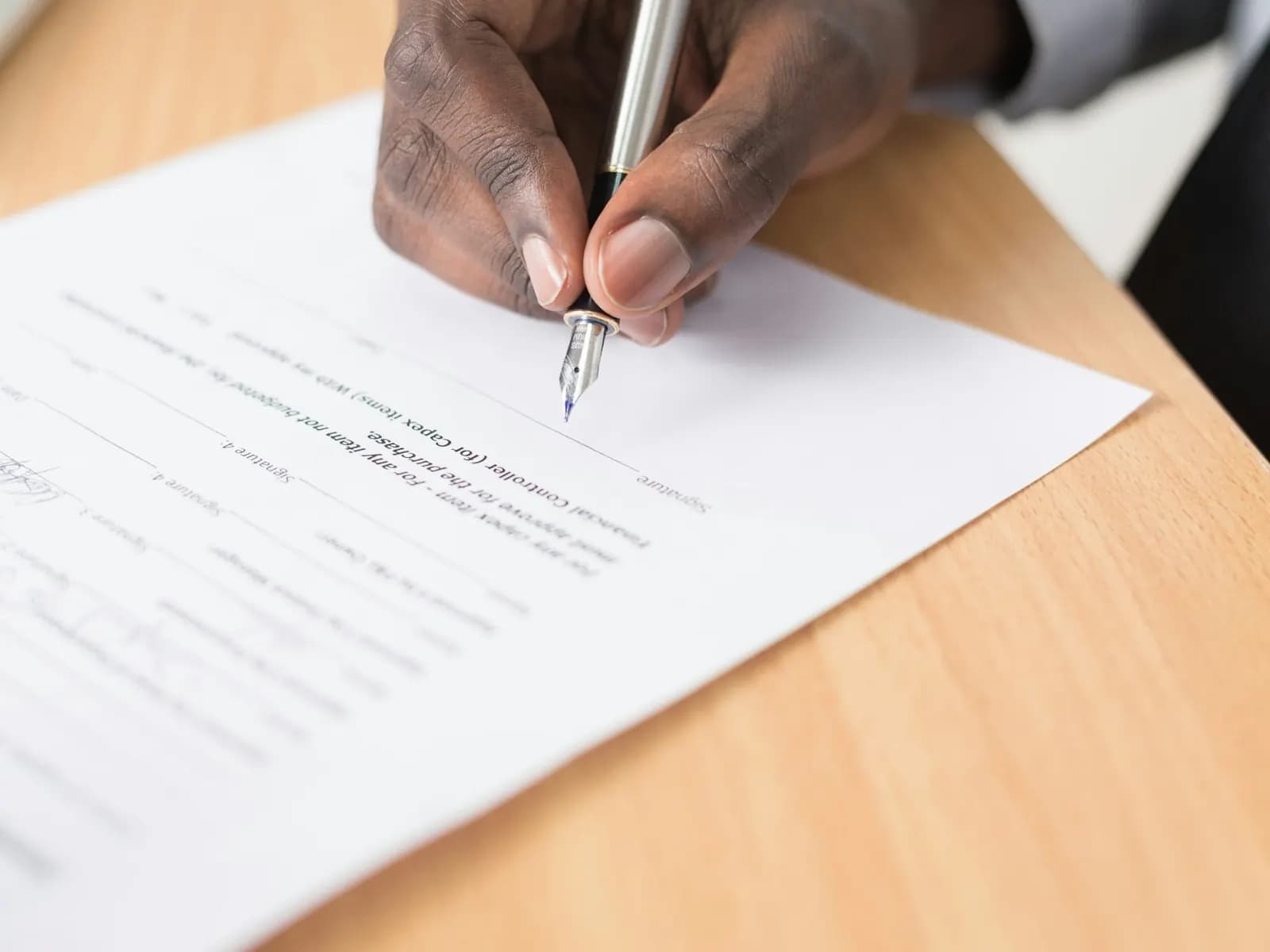 A hand signing a printed agreement with a fountain pen