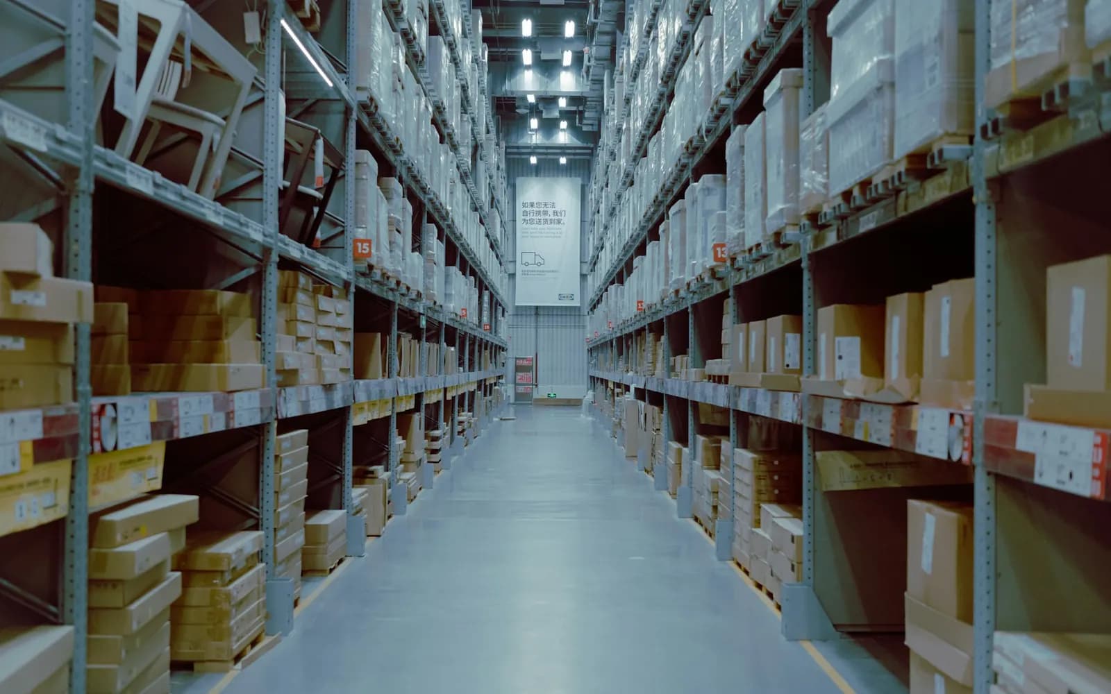 A long warehouse aisle of steel racking stocked with uniform cardboard cartons